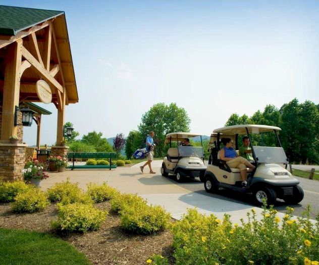 People are riding golf carts near a building surrounded by lush greenery and a well-maintained garden pathway.