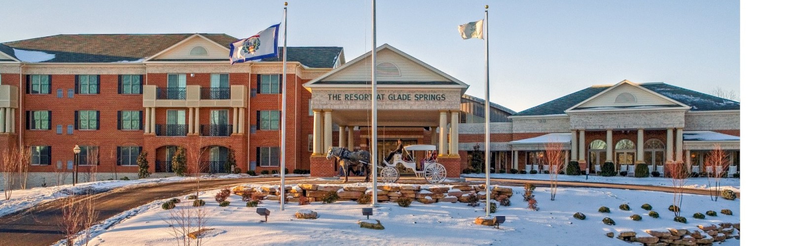 The image shows a large brick building with a snow-covered landscape, featuring a few flags and a circular driveway at the entrance.