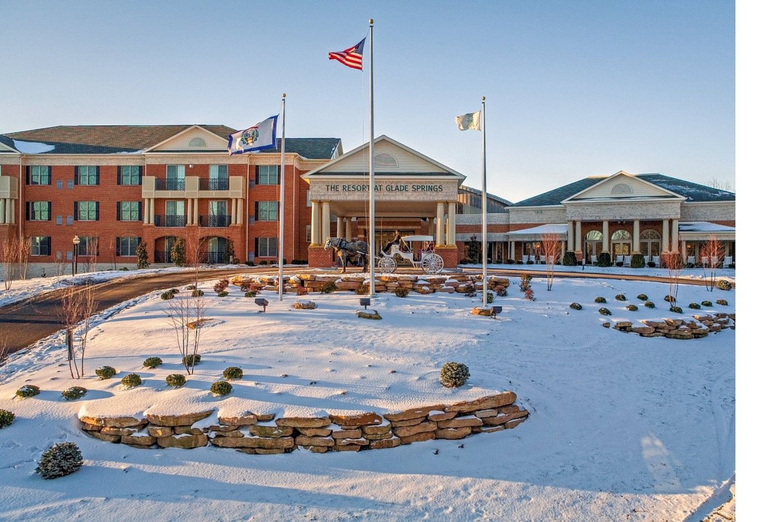 A large building with American and two other flags, surrounded by snow and landscaping, under a clear blue sky.