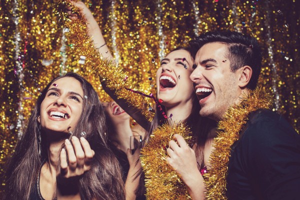 People are joyfully celebrating, surrounded by gold tinsel and confetti, with big smiles and festive attire in the image.