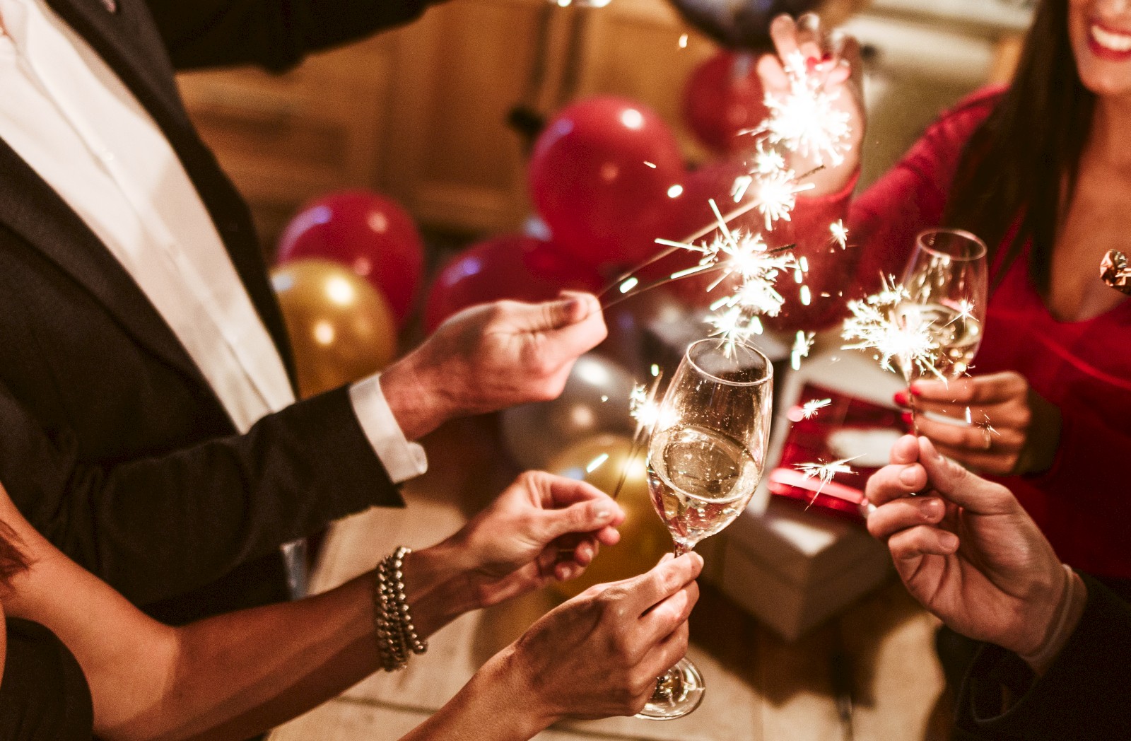 People holding sparklers and champagne glasses, celebrating with balloons in the background.