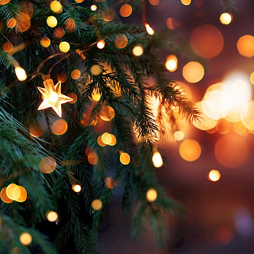A Christmas tree with star-shaped lights, surrounded by a bokeh effect of warm glowing lights, creating a festive ambience.