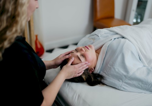 A person is receiving a facial massage while lying on a massage table, covered by a blanket in a serene room setting.