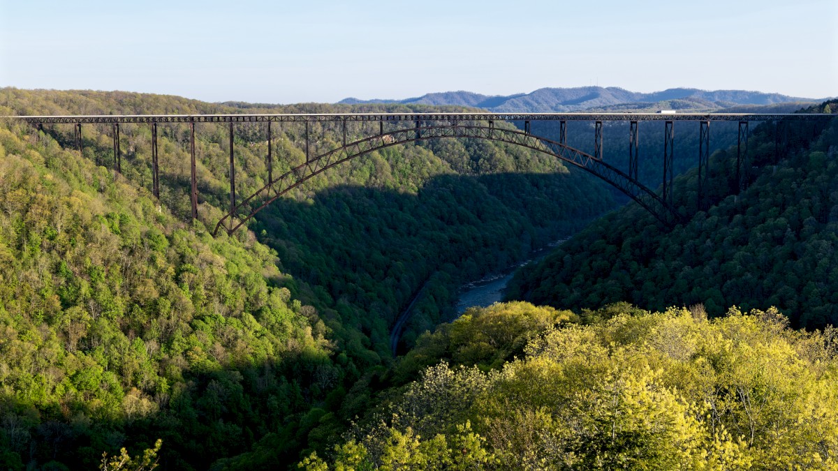 A large arched bridge spans over a lush, green valley with a river running below, surrounded by forested hills.