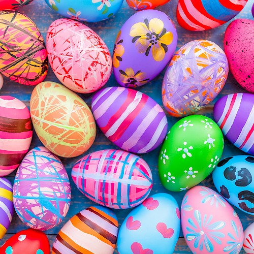 A collection of colorful, intricately decorated Easter eggs in various patterns and designs are spread out on a surface.