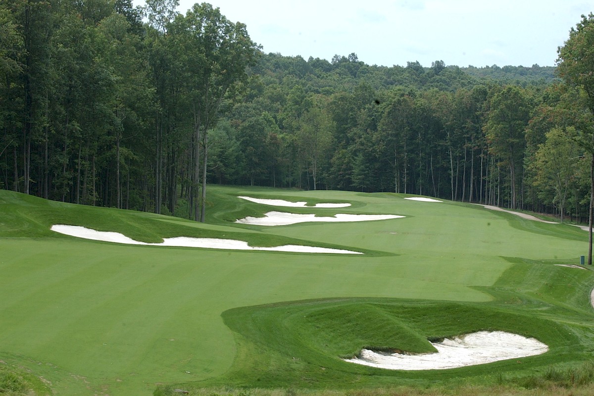 A lush golf course fairway with several sand bunkers and a tree-lined backdrop, rolling greens and a winding cart path.