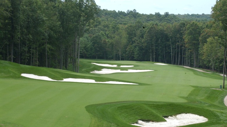 A lush golf course fairway with several sand bunkers and a tree-lined backdrop, rolling greens and a winding cart path.