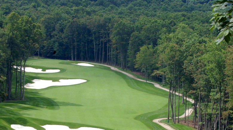A scenic golf course with lush green fairways, sand bunkers, and tall trees lining a winding layout at a sunny risk.