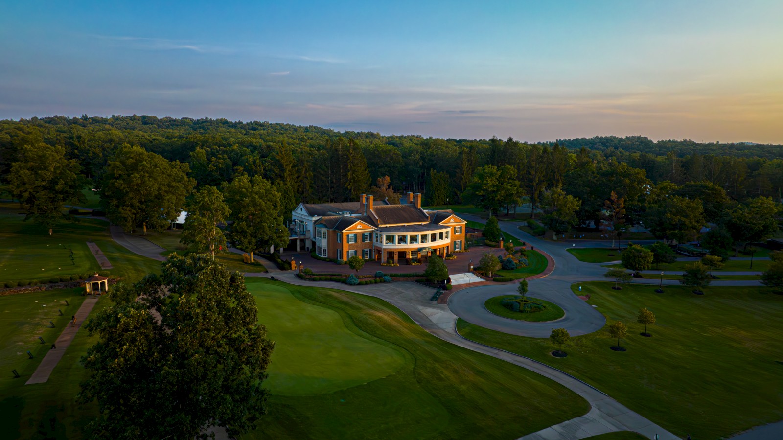 An aerial view of a large building surrounded by lush greenery and a golf course, with a circular driveway in front.