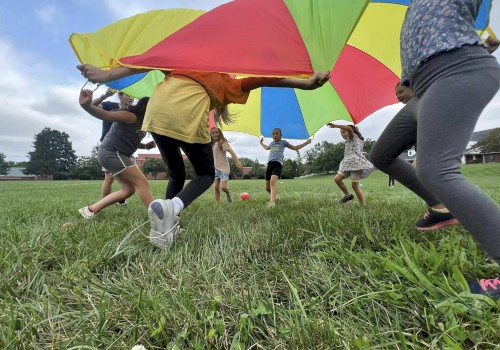 Children playing outside with a colorful parachute on a grassy field, smiling and having fun together.
