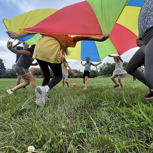 Children playing outside with a colorful parachute on a grassy field, smiling and having fun together.