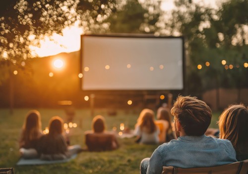 People watching a movie outdoors on a lawn at sunset, surrounded by trees and string lights.