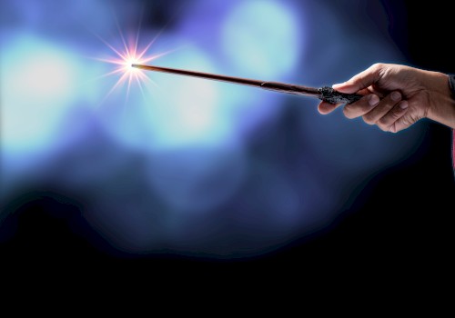 A hand holds a wand or magic wand with a sparkling light at its tip, against a dark, blurred blue background.
