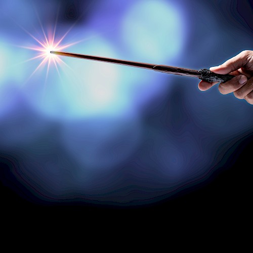 A hand holds a wand or magic wand with a sparkling light at its tip, against a dark, blurred blue background.
