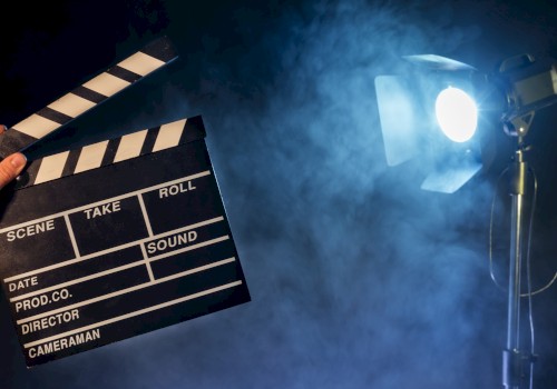 A behind-the-scenes film set scene: a clapperboard in hand, studio lights, and smoky atmospheric glow ready for filming. Ending with a period.