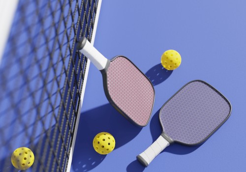 Two pickleball paddles and three yellow balls are on a blue court next to a net.