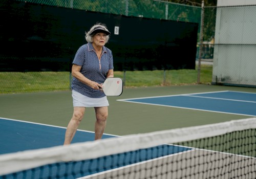 A person is playing pickleball, wearing a visor and holding a paddle on an outdoor court near a net, focusing on the game.