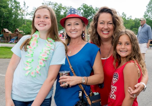 Four people are smiling at an outdoor event, with two adults and two children in casual attire.