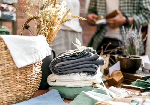 A display featuring folded linens, a basket with dried flowers, and a person in the background holding an item, outdoors.