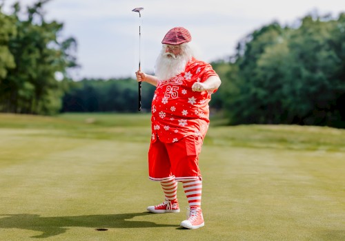 A person dressed in festive attire, resembling Santa, is playing golf on a green, with a putter in hand.