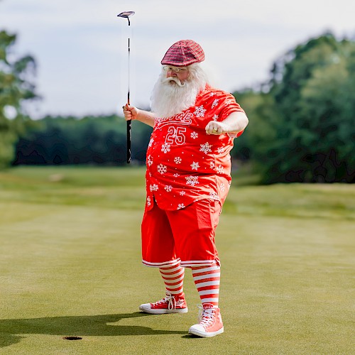 A person dressed in festive attire, resembling Santa, is playing golf on a green, with a putter in hand.