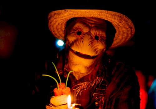 A man wearing a straw hat holds a lit sparkler, smiling in a dark, festive scene.