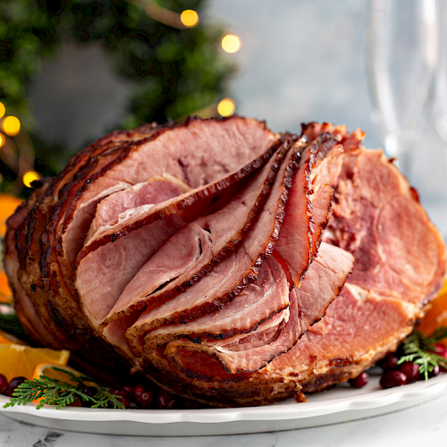 A sliced roasted ham centerpiece on a plate, garnished with orange slices and herbs, festive background lights, flavorful and juicy.