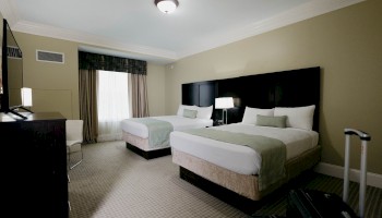 This is a hotel room with two beds, a TV, a window, and a suitcase near the bed.