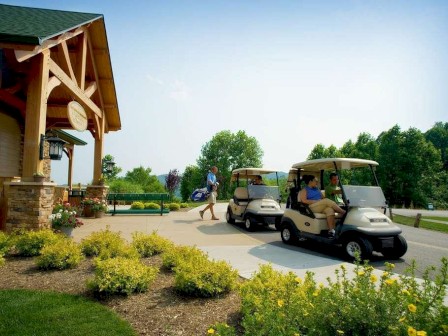 A wooden building with people in golf carts on a sunny day, surrounded by greenery and landscaped plants.