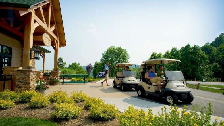 People are using golf carts outside a clubhouse surrounded by greenery and landscaping.
